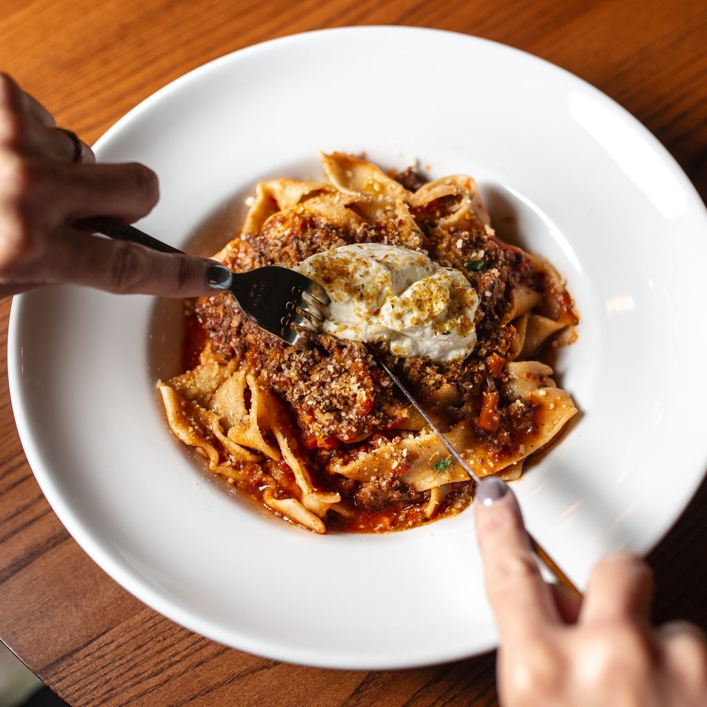 Elk & Bone Marrow Ragu Pappardelle Guest cutting with a knife and fork, the Elk & Bone Marrow Ragu Pappardelle served in a dish