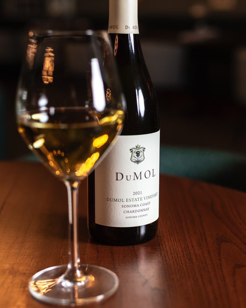 A glass of DuMol Chardonnay next to the bottle of wine
