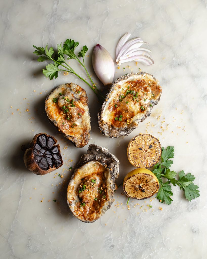Black Garlic Miso Oysters (broiled), surrounded by ingredients (shallot, cilantro, black garlic)