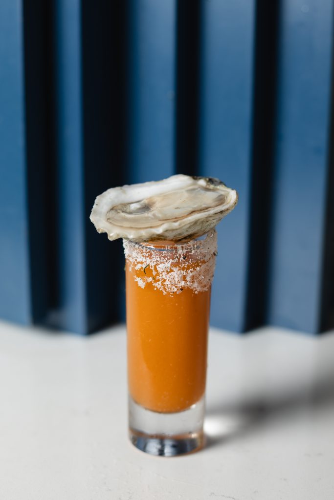 Tipsy Oyster Shooter in a shot glass, with a fresh shucked oyster sitting on top of the glass